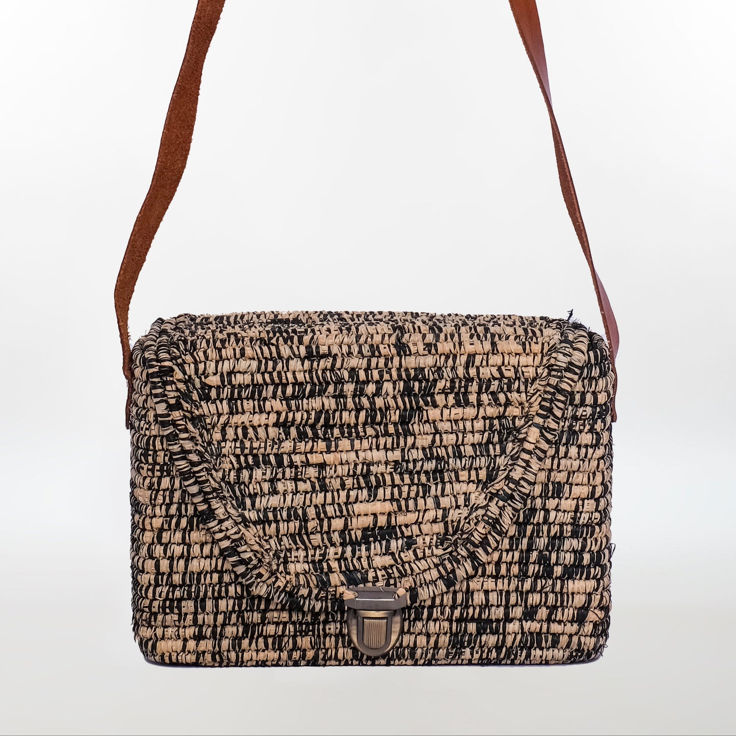 Black and natural raffia crossbody bag with boxy shape, metal clasp, and leather strap