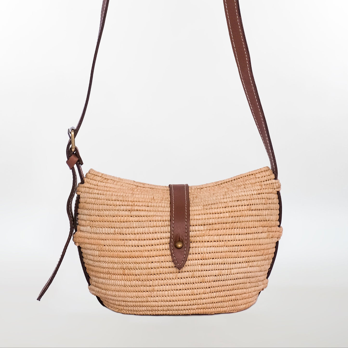 Handwoven raffia crossbody bag with brown leather strap and button closure