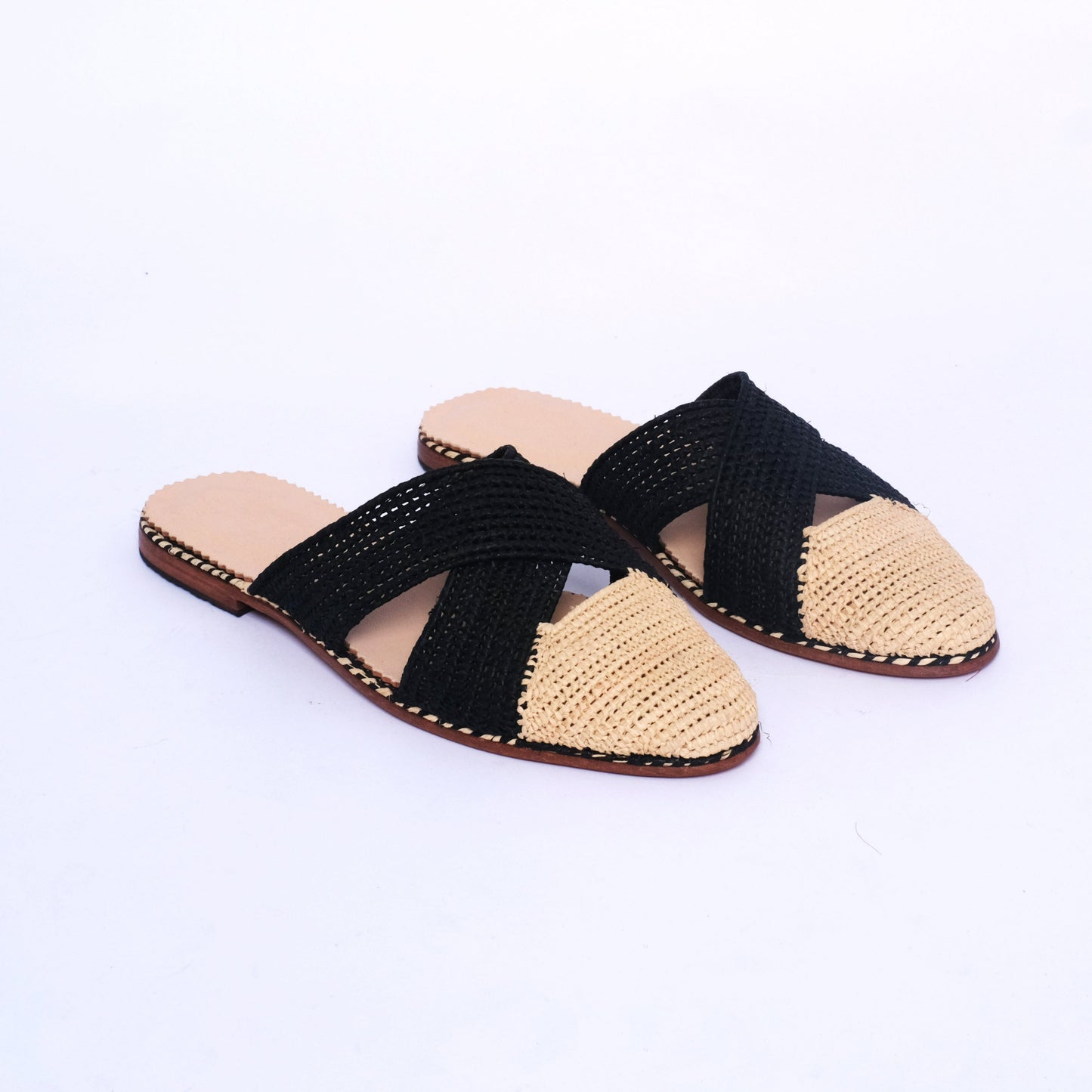 Women’s handmade raffia slide mules featuring black woven crossover straps and a natural raffia front, flat leather sole, crafted in Morocco.