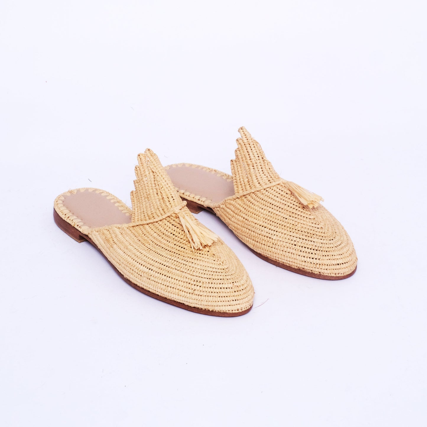 Women’s handmade raffia mules with a scalloped tongue and raffia tassel, pointed toe, and flat leather sole, crafted in Morocco.