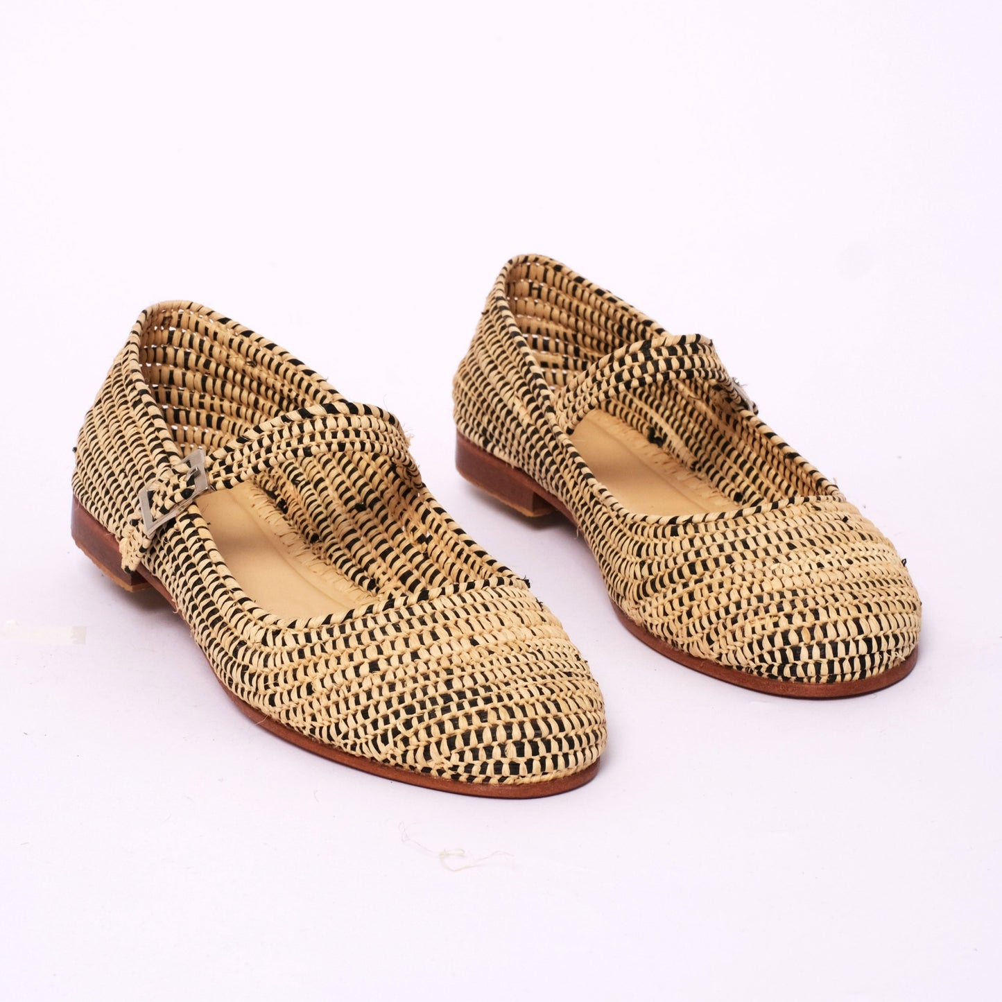 Handwoven women’s Mary Jane flats made from black and natural raffia, featuring a two-tone woven design, leather sole, and adjustable strap, handmade in Morocco.