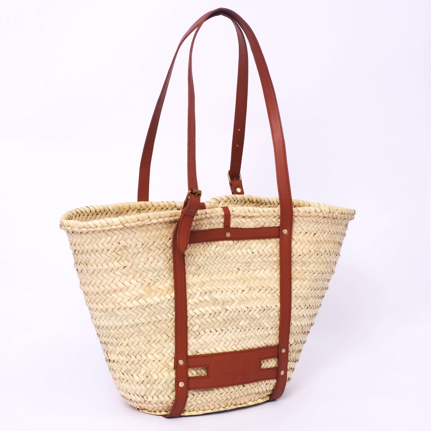 Moroccan straw tote with full harness-style leather straps, buckles, and brass hardware, photographed against a white background.