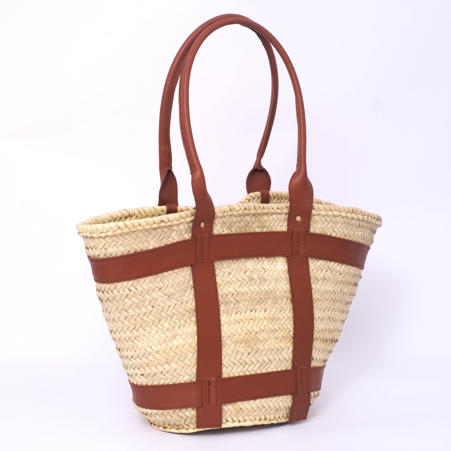 Small round Moroccan straw crossbody bag with tooled leather handles, branded leather tag, and adjustable strap, photographed on a white background.