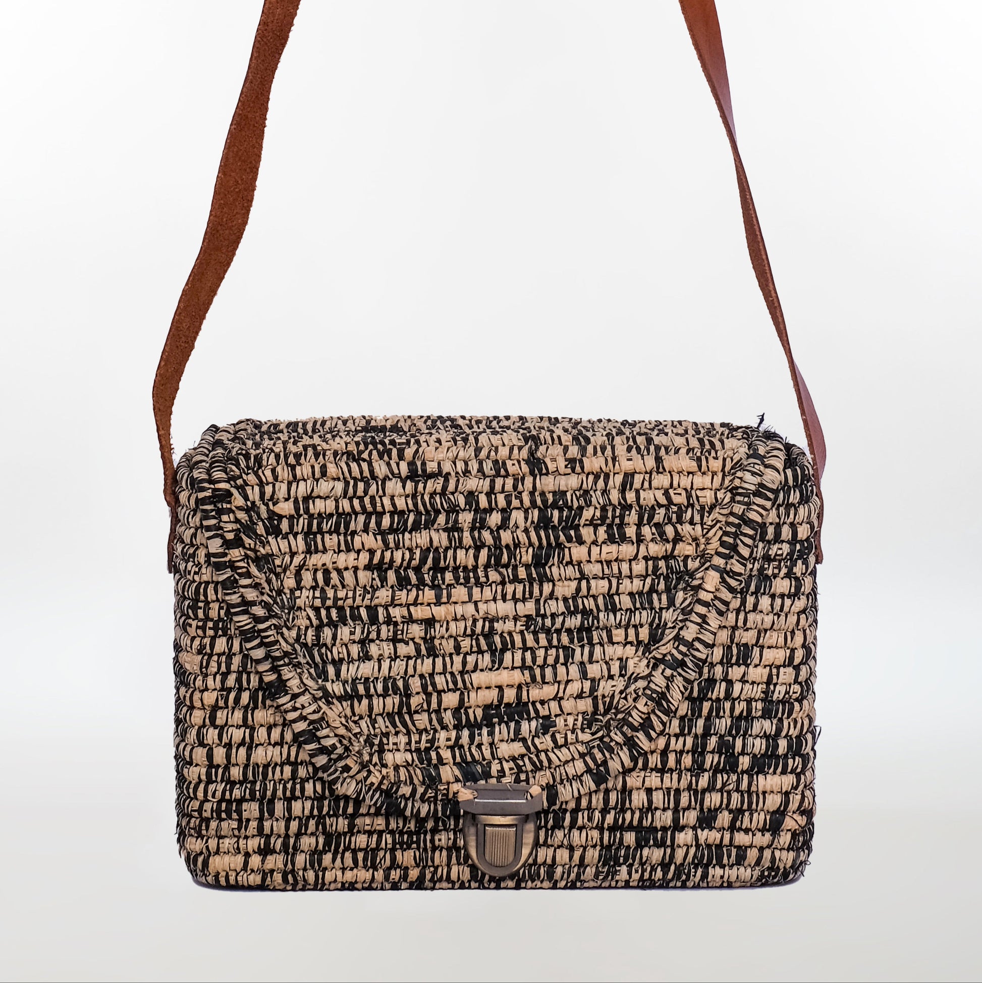 Black and natural raffia crossbody bag with boxy shape, metal clasp, and leather strap