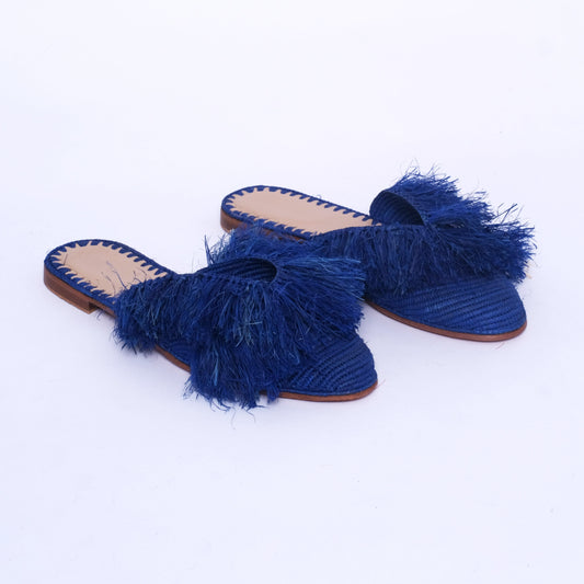 Women’s royal blue raffia mules with oversized fringe detailing, flat leather sole, and handwoven Moroccan artisan construction.