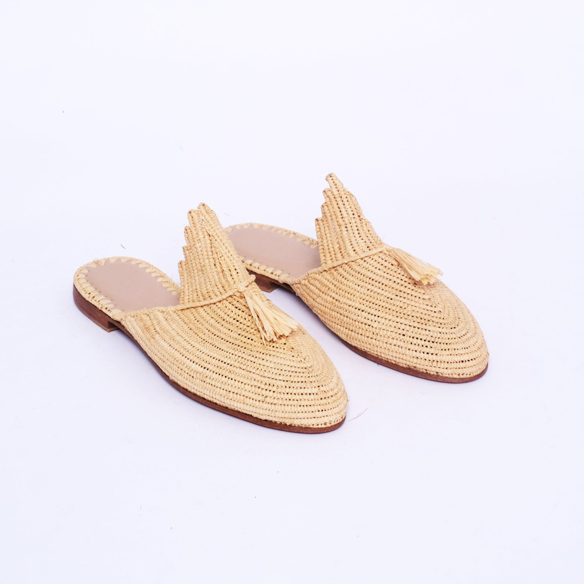 Women’s handmade raffia mules with a scalloped tongue and raffia tassel, pointed toe, and flat leather sole, crafted in Morocco.