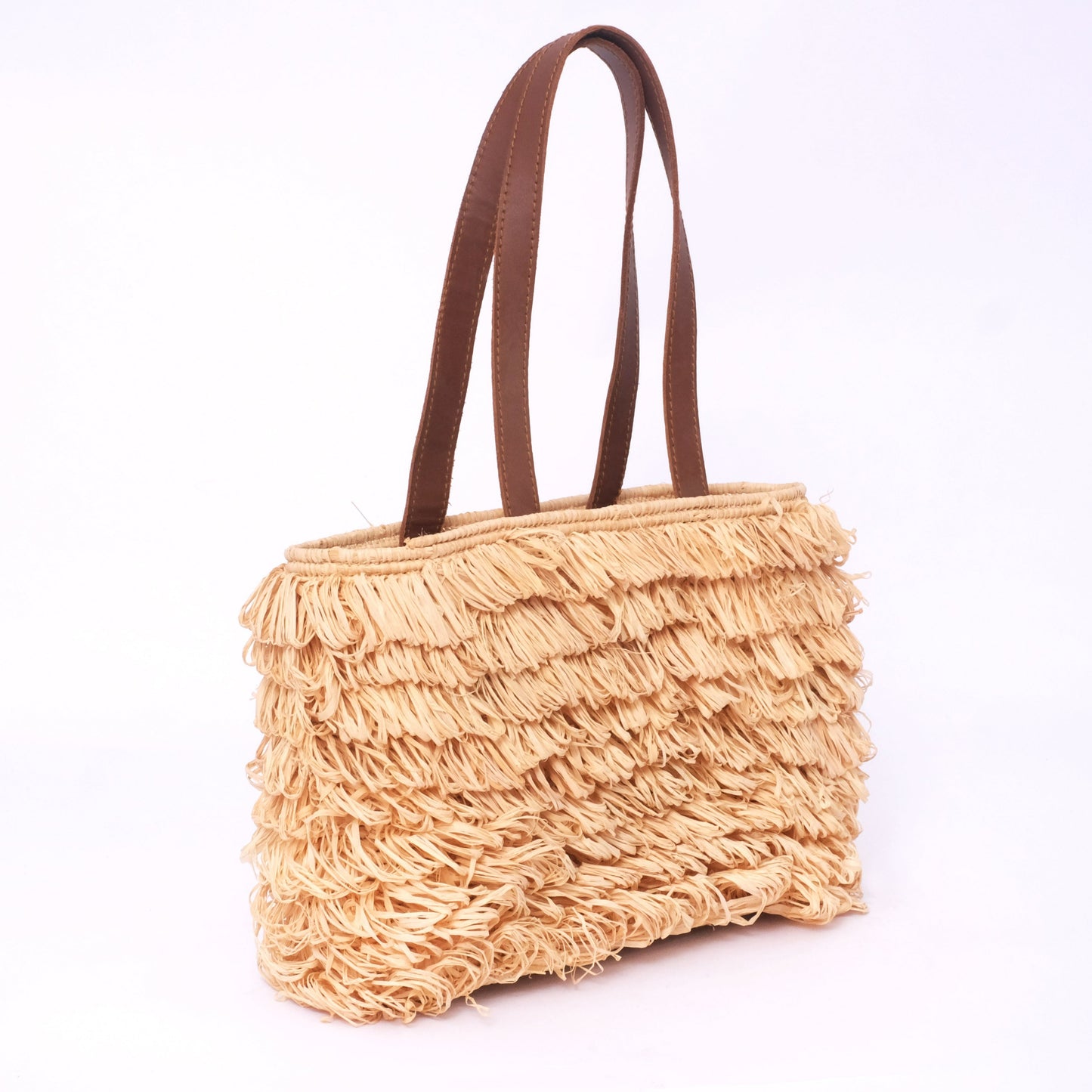 Fringed raffia tote bag with long brown leather handles and layered texture