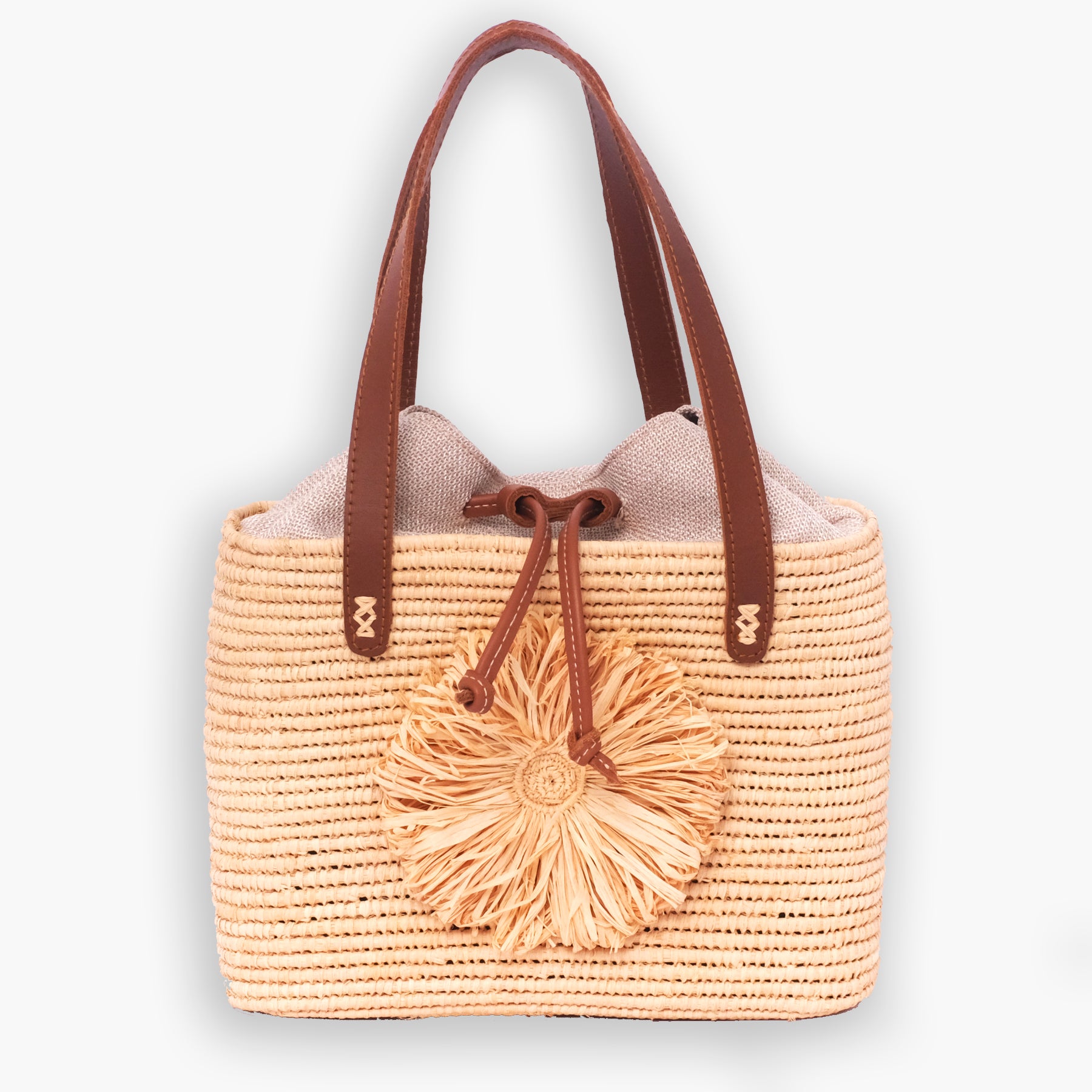 Handwoven raffia tote bag with leather handles, drawstring linen top, and raffia flower accent